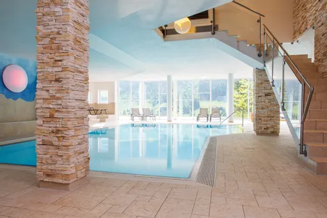 Modernes Hallenbad im Hotel mit Liegestühlen und großen Fenstern mit Blick auf grüne Berge